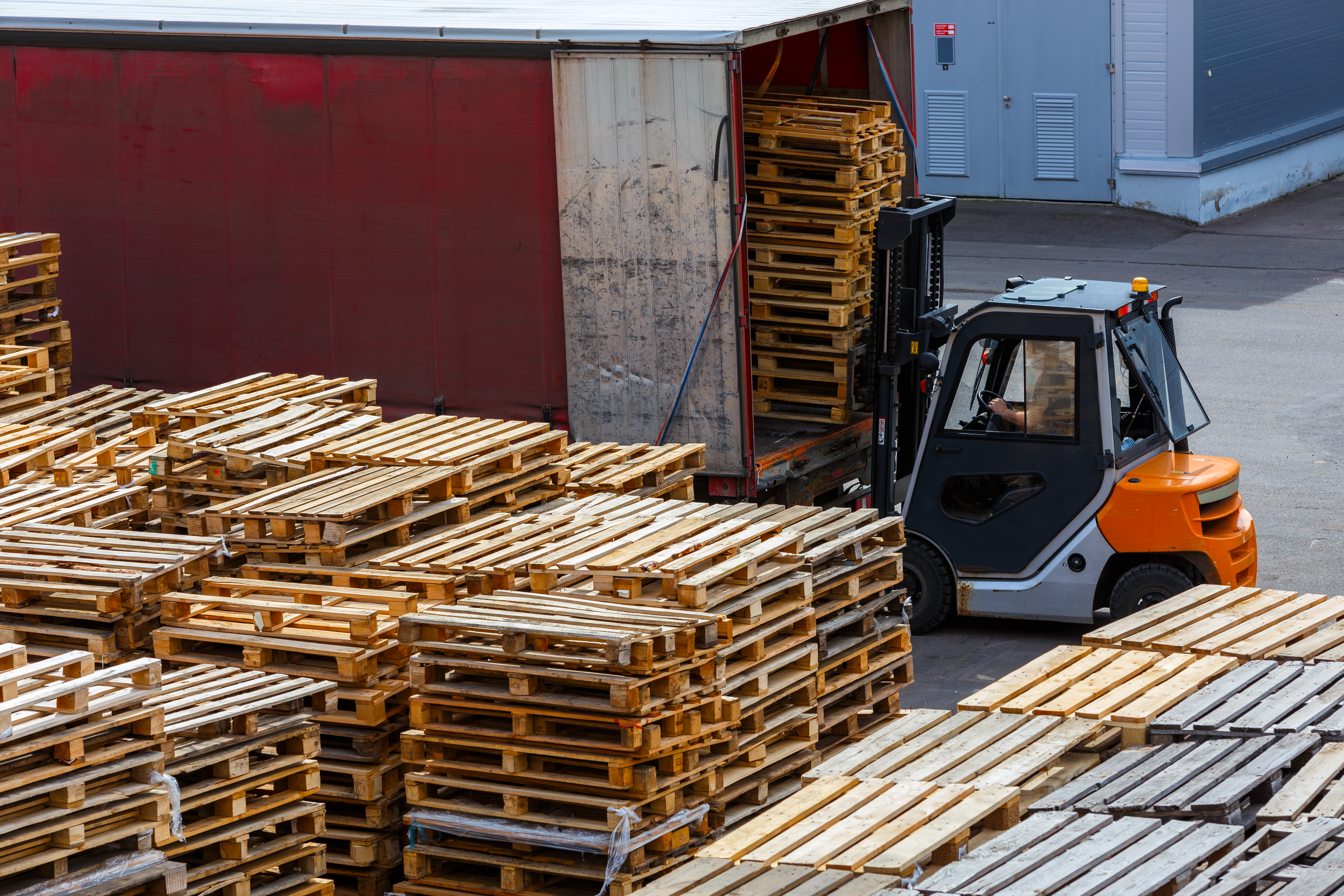forklift loading used wooden pallet stacks into truck - perspective view from above.